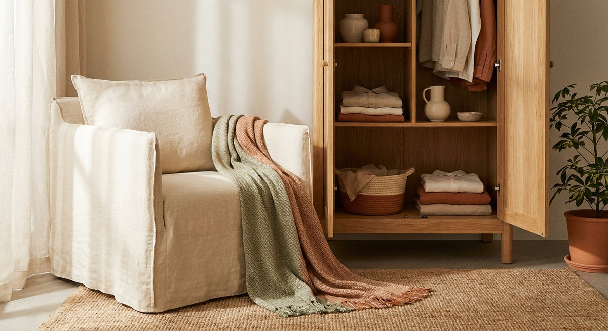 A sunlit room corner where an open wardrobe and a linen armchair share a cohesive palette of ivory, sage, and terracotta, unified by natural textures and warm afternoon light.